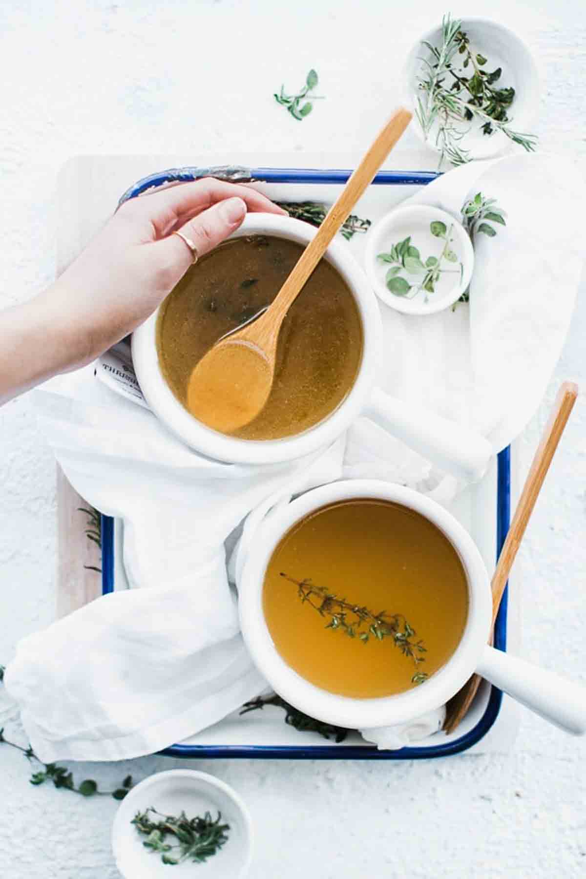two bowls of broth with a hand around one of them