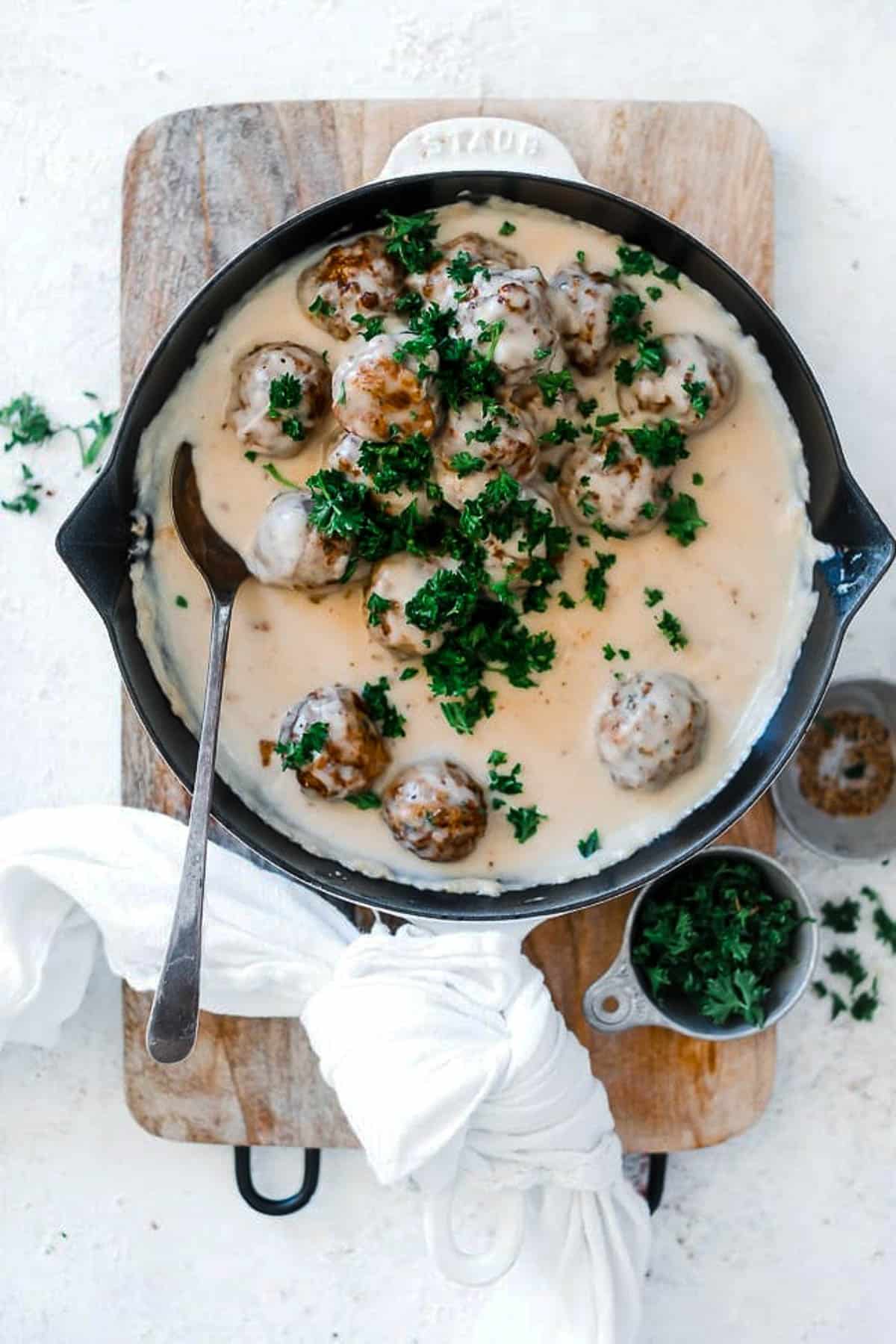 Easy Swedish meatball recipe in a cast iron skillet, atop a wooden cutting board and garnished with parsley.