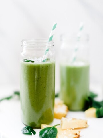 Green protein Pina colada smoothie in a glass with a straw.
