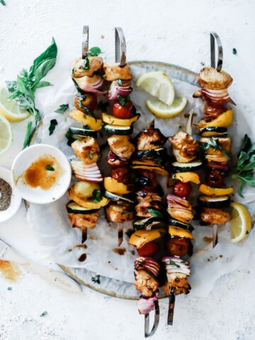 Honey Mustard Chicken Kabob Marinated skewers on a silver platter. Skewers are arranged straight up and down. The platter is garnished with lemons are basil.
