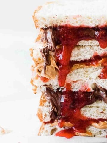 Strawberry freezer jam on a peanut butter sandwiches cut in half and stacked on top of each other.