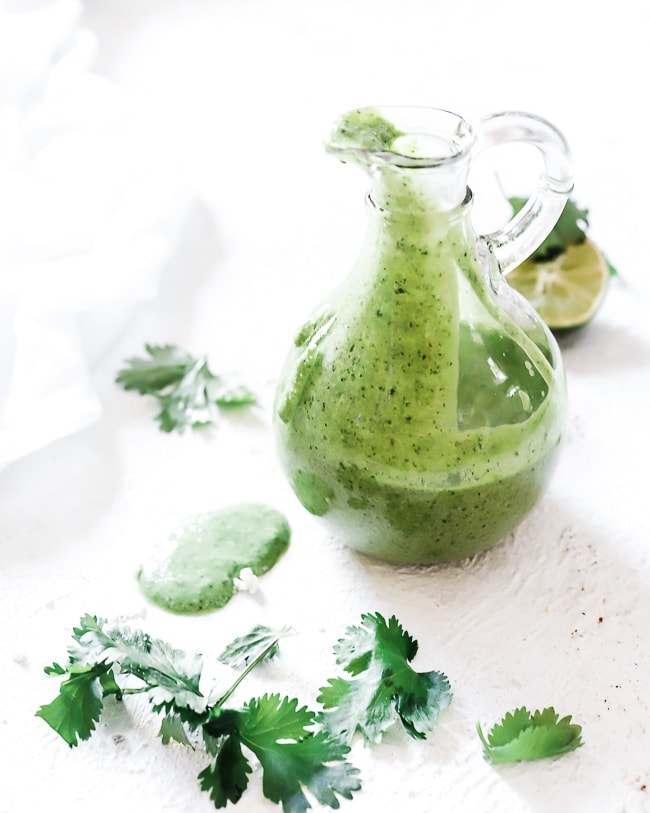 Lime cilantro dressing in a glass container, style with cilantro leaves and squeezed limes.