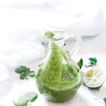 Lime cilantro dressing in a glass container, style with cilantro leaves and squeezed limes.
