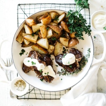 Easy pan fried lamb chops in a white braiser filled with roasted potatoes. The chops are topped with feta cream sauce and garnished with parsley.