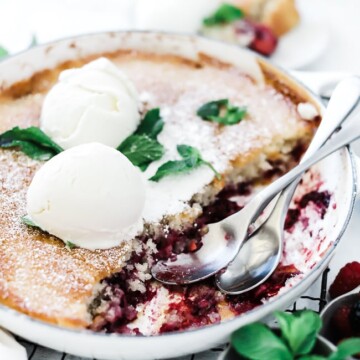 Berry Cobbler recipe in a white braiser. The pan is set atop a wire cooling rack and is garnished with mint and ice cream.