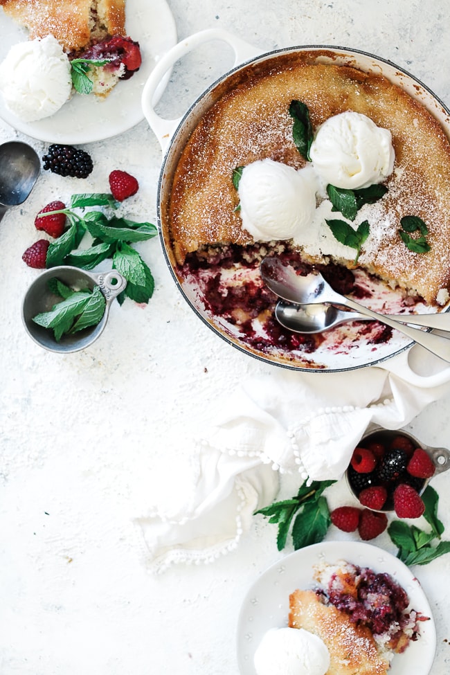 Lemon Berry Cobbler in a white braiser. There are berries and mint surrounding the braiser.