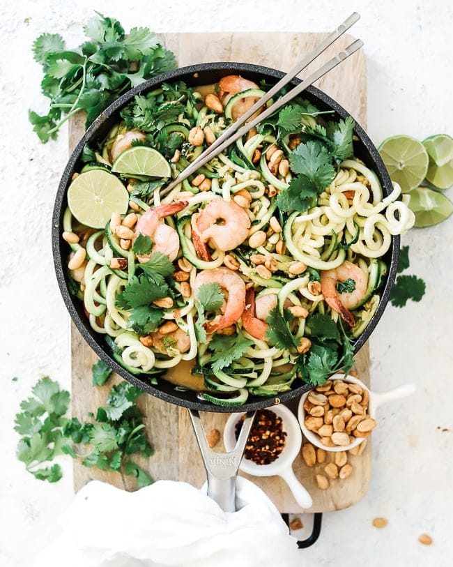 A birds eye view of shrimp pad Thai recipe. The dish is prepared in a skillet which is resting atop a wooden cutting board.