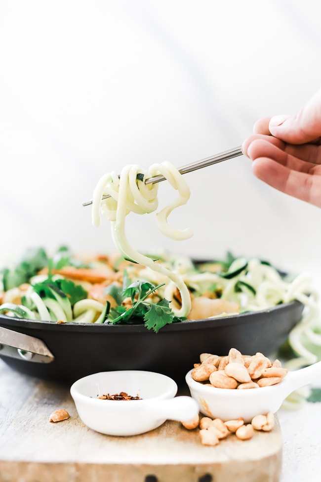 Zoodles being lifted out of a pan with chopsticks.
