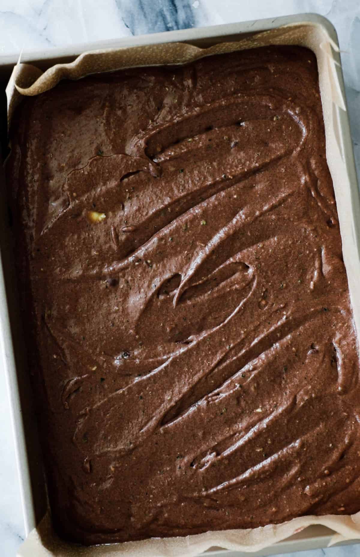 Chocolate zucchini cake batter in a lined with parchment paper.