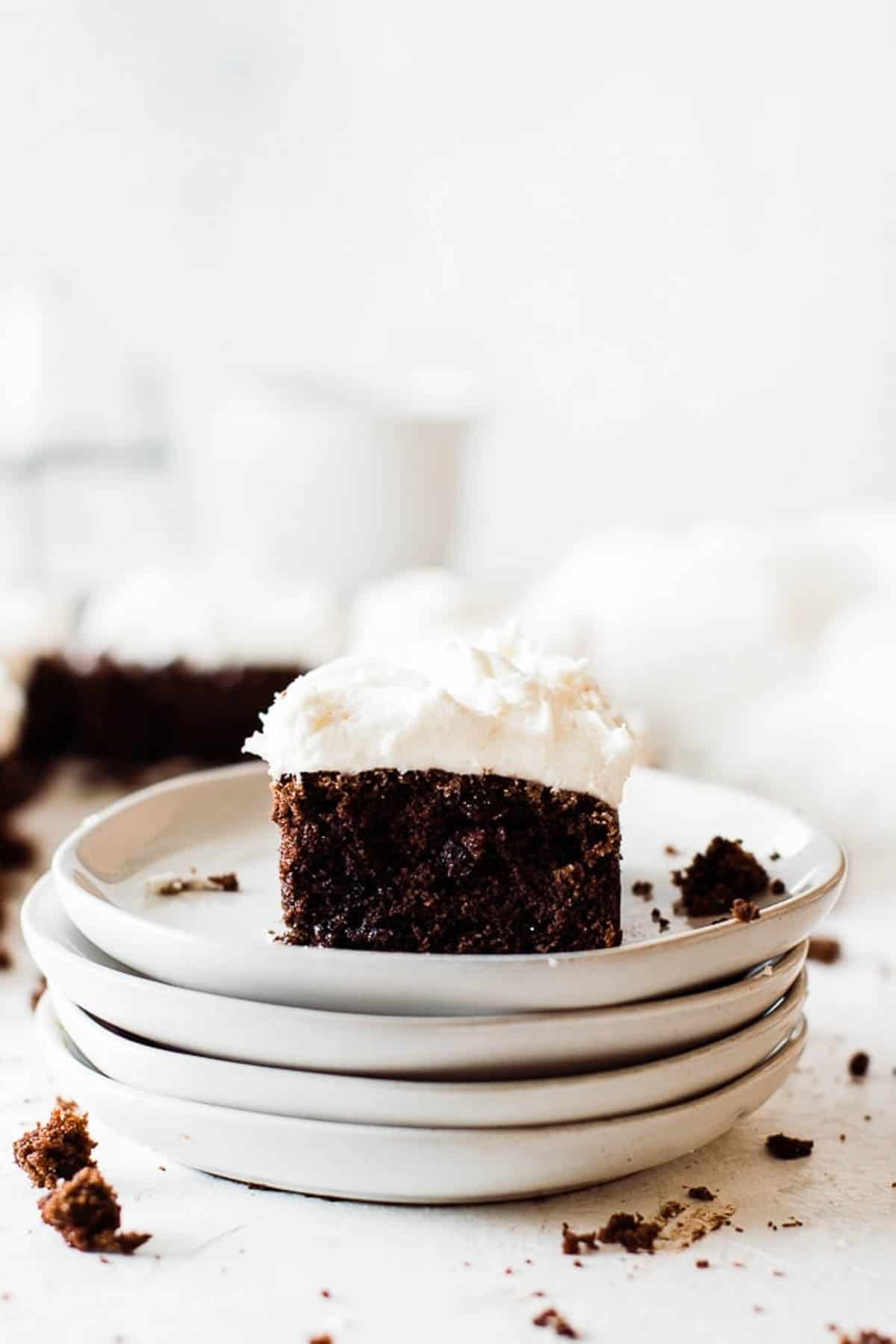 One slice of chocolate zucchini cake on a stake of plates frosted high with cream cheese frosting.