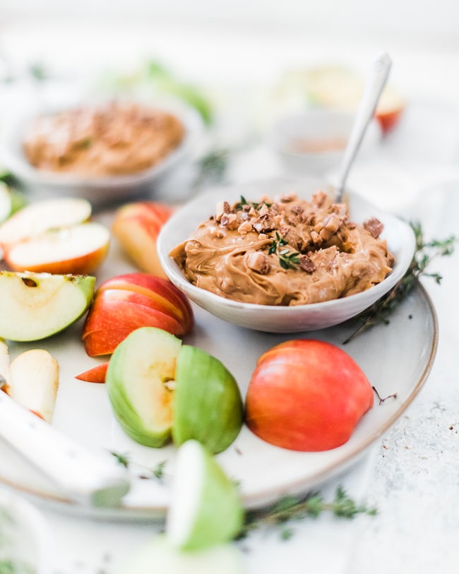 a ¾ view of toffee apple dip in a grey bowl. It is surrounded by sliced apples on a plate.
