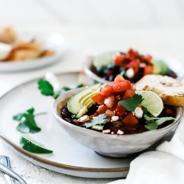 A ¾ view of black bean soup garnished with avocado, pico, feta cheese and lime.