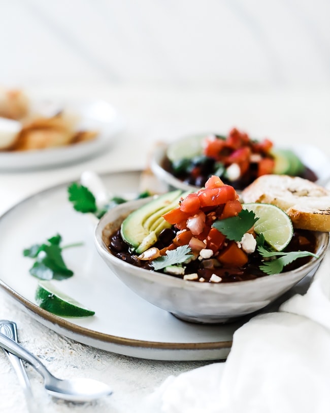 A ¾ view of black bean soup garnished with avocado, pico, feta cheese and lime.