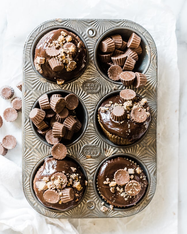 Chocolate peanut butter cupcakes in a metal cupcake tray. Some cups are filled with mini peanut butter cups.
