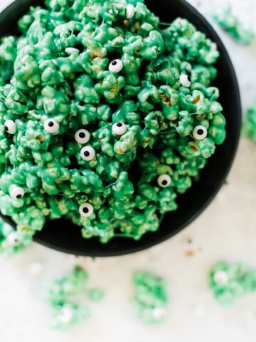 Monster halloween popcorn in a large black bowl. The popcorn is green with candy eyeballs.