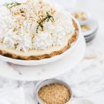 A ¾ view of banana cream pie. The pie is garnished with whipped cream and green flowers.