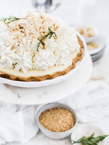 A 3/4 view of banana cream pie. The pie is garnished with whipped cream and green flowers.