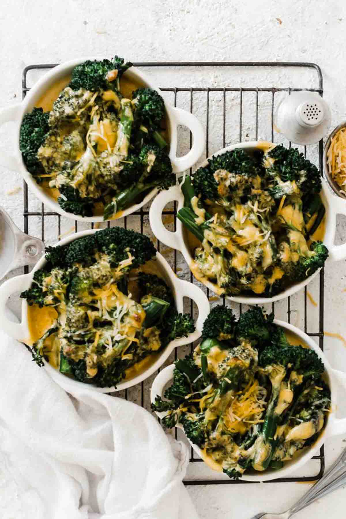Small dishes of broccoli and cheese sauce on a cooling rack.