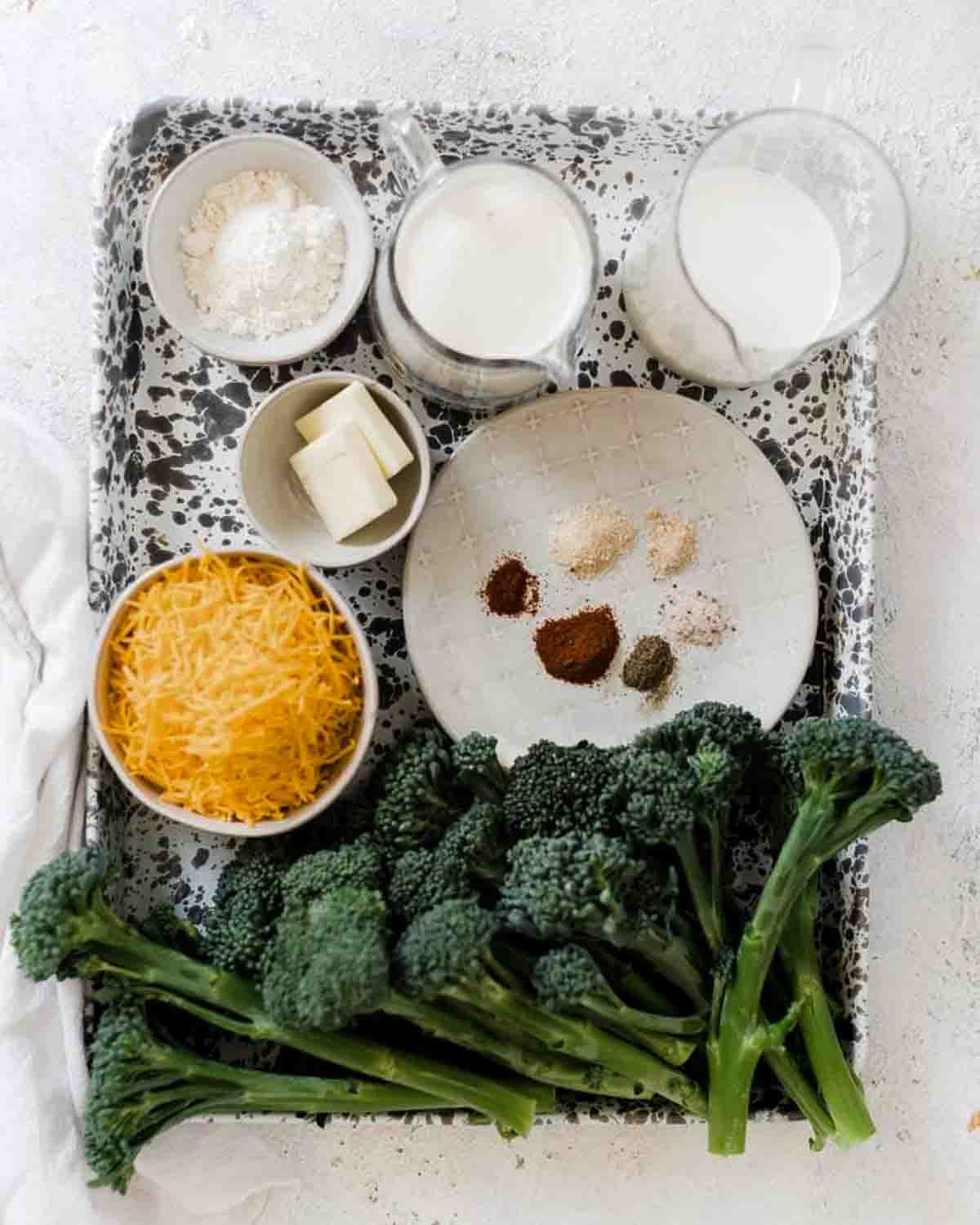Ingredients needed to cook broccoli and cheese sauce on a marbled baking sheet.