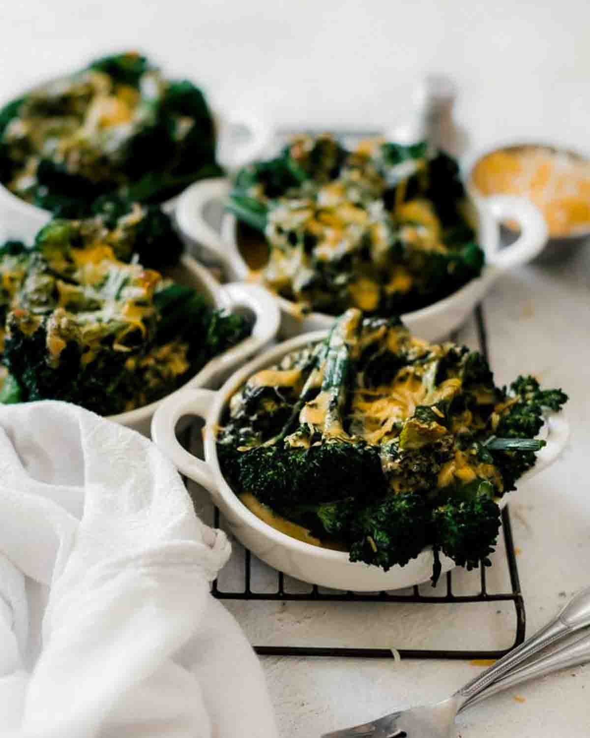 Small dishes of broccoli and cheese sauce on a cooling rack.