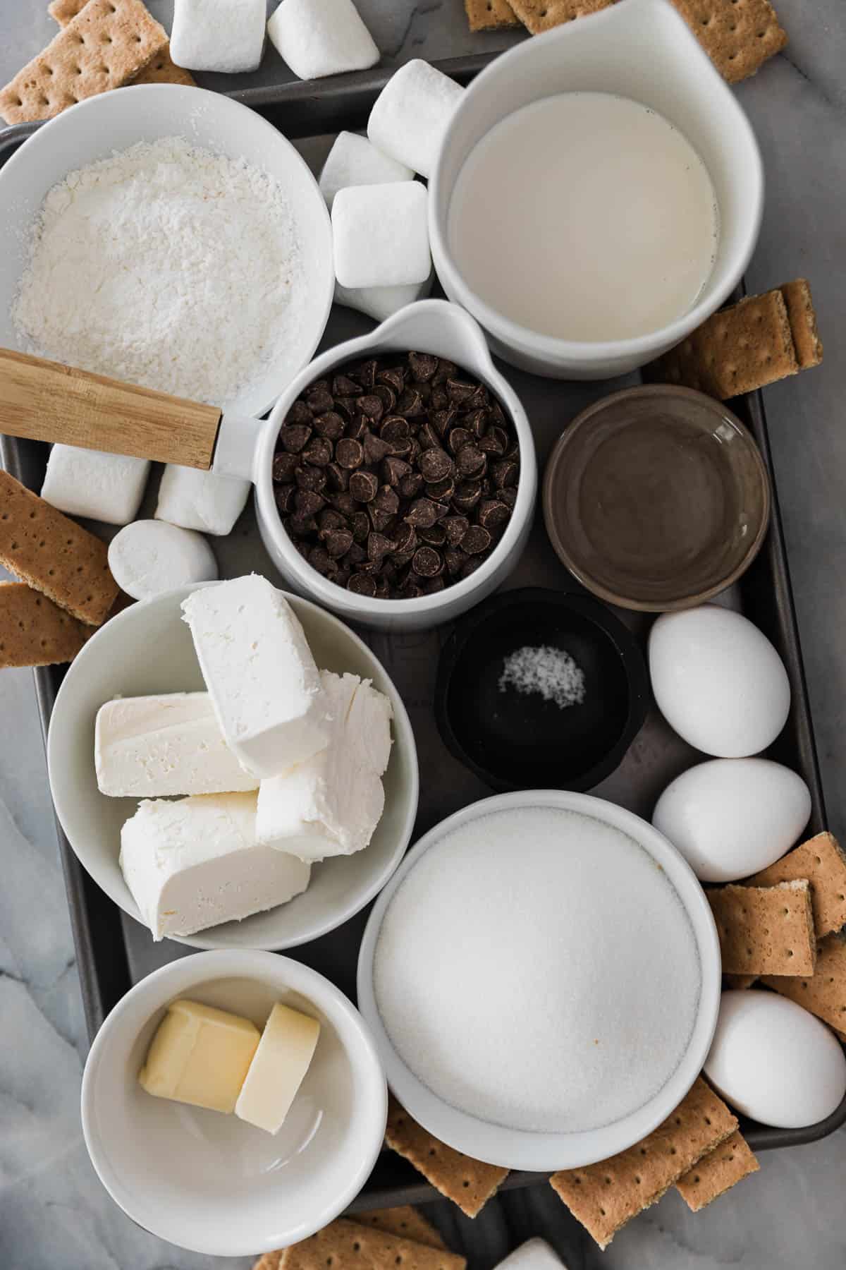 Ingredients of cream cheese, marshmallows, eggs, sugar, chocolate chips and so on on a tray to make s'mores pie. 