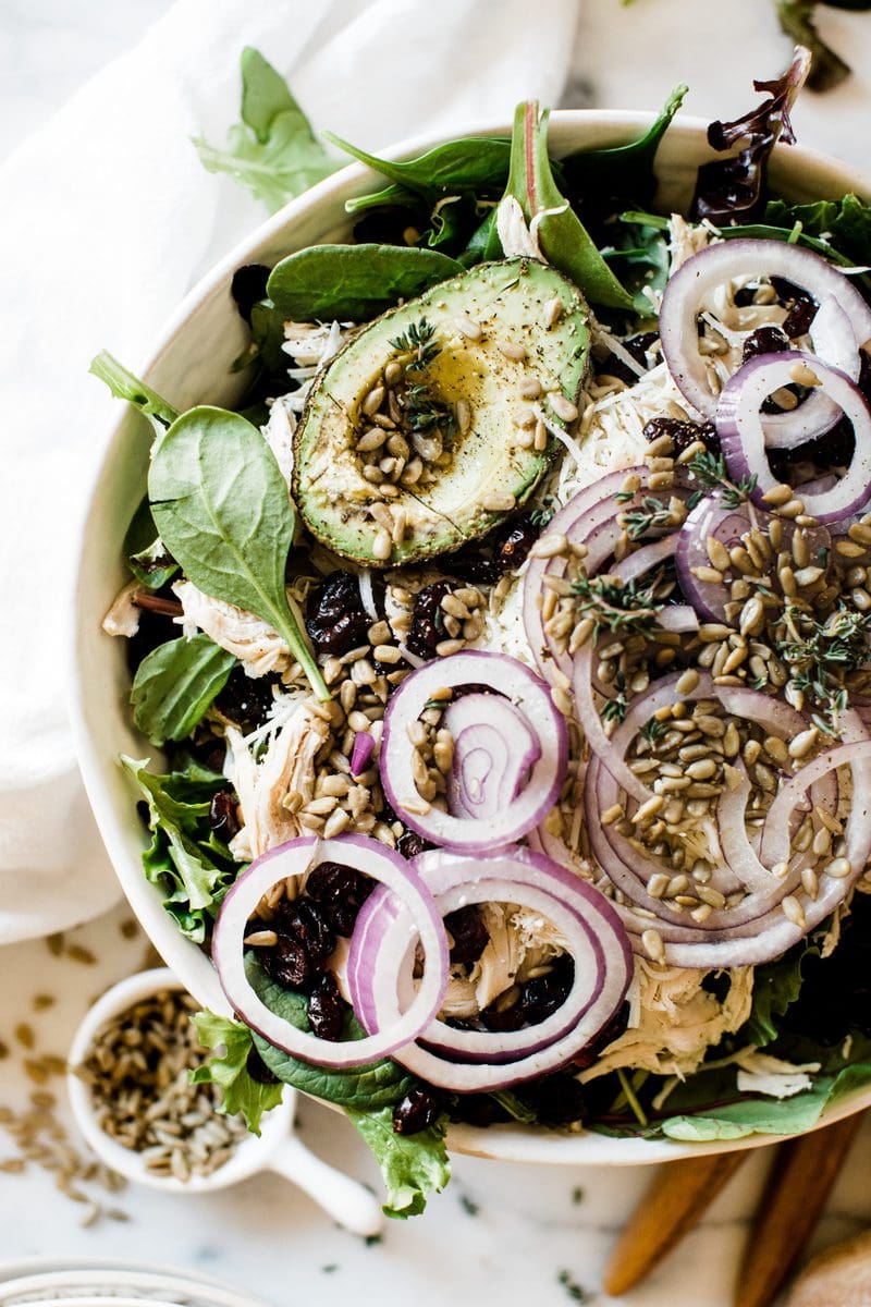 A close up of Kneader turkey salad. It is garnished with red onion and there is a small bowl of sunflower seeds to the side.
