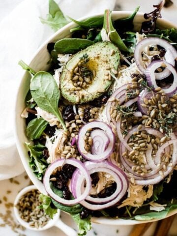 A close up of Kneader turkey salad. It is garnished with red onion and there is a small bowl of sunflower seeds to the side.