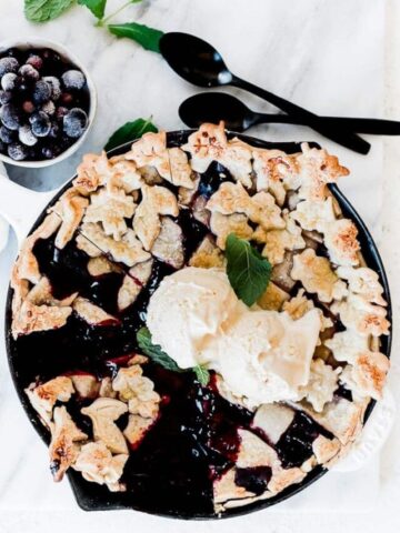 Razzleberry pie in a white skillet topped with vanilla ice cream.