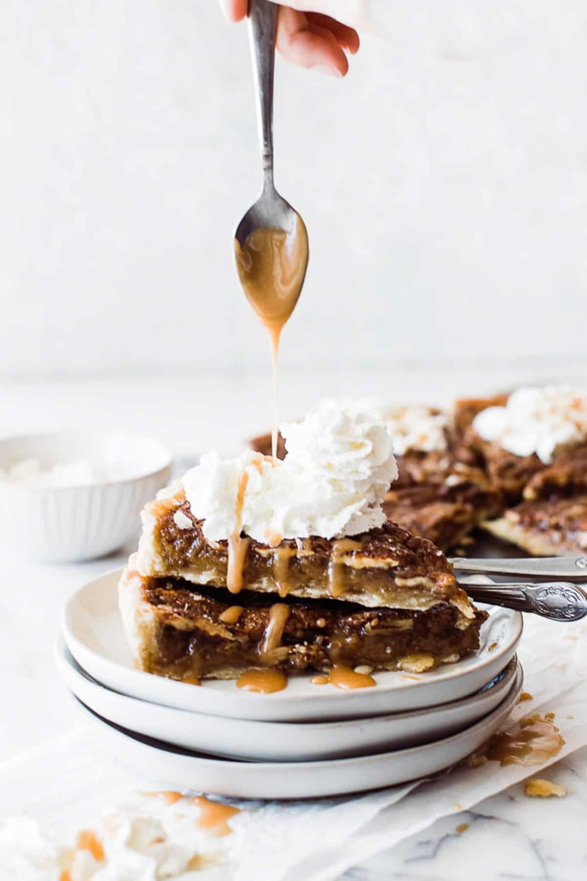Spoon drizzling caramel sauce on two pieces of pecan pie