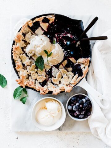 Razzleberry pie in a white skillet. there is a small bowl of ice cream to the side.