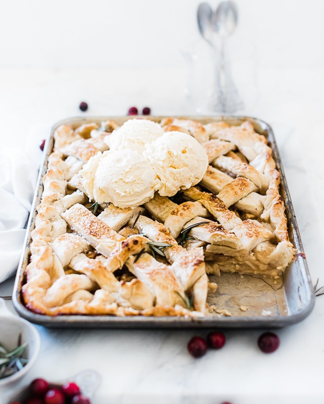A ¾ angle shot of apple slab pie. The pie is baked in a sheet pan with one slice missing. There are 3 scoops of ice cream on top.