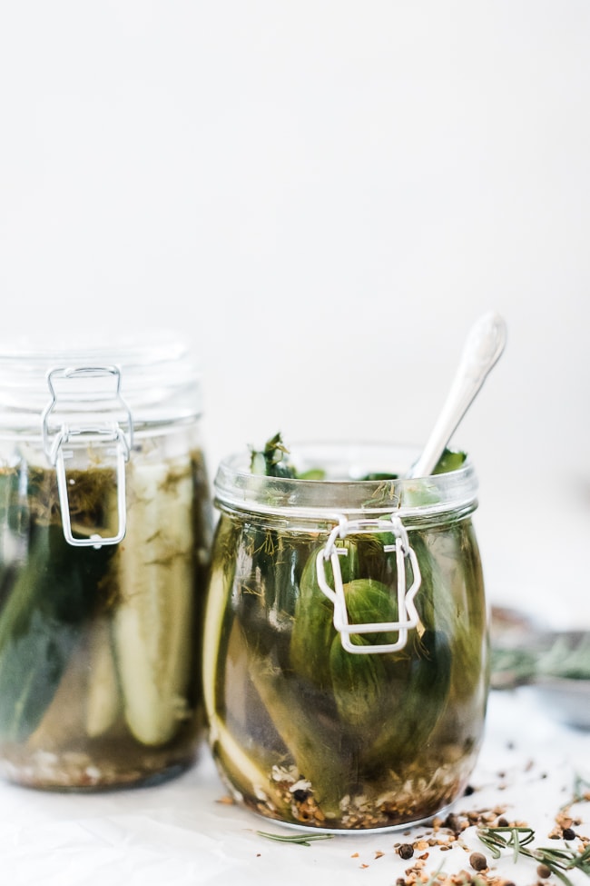 Two glass jars filled with dill pickles. One is open with a fork inserted.