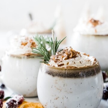 Coconut milk hot chocolate in white mugs. They are topped with whipped cream and garnished with rosemary.