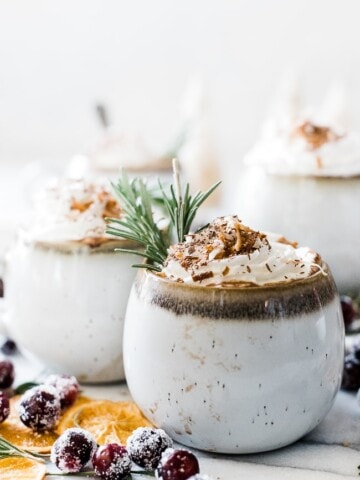 Coconut milk hot chocolate in white mugs. They are topped with whipped cream and garnished with rosemary.