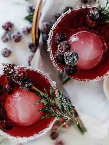 Glasses of sparkling cranberry mocktails with the rim sugared on a copper tray.