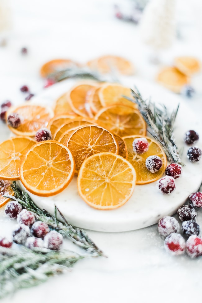 Dried orange slices on a marble tray surrounded by sugared cranberries and rosemary.