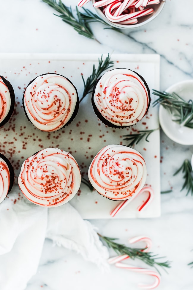 An overhead shot of peppermint chocolate cupcakes. The cupcakes are on a marble platter and there is rosemary scattered around.