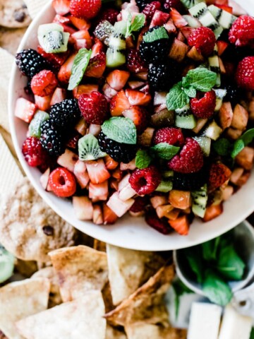 A close up of fruit salsa in a white bowl. The salsa is garnished with mint.