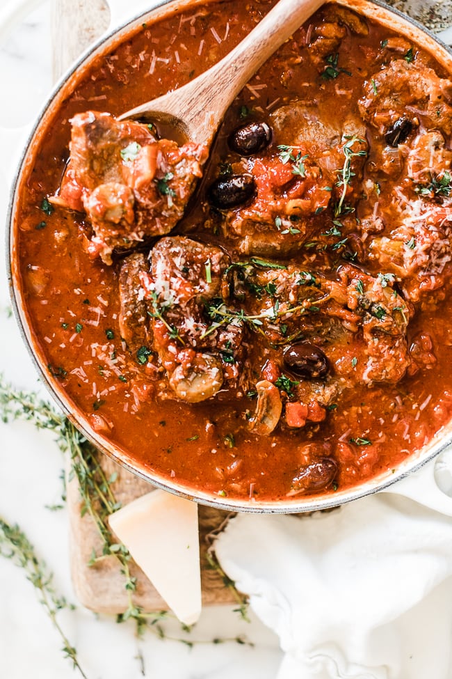 Lamb cacciatore recipe in a white braiser, it is garnished with olives and fresh thyme.