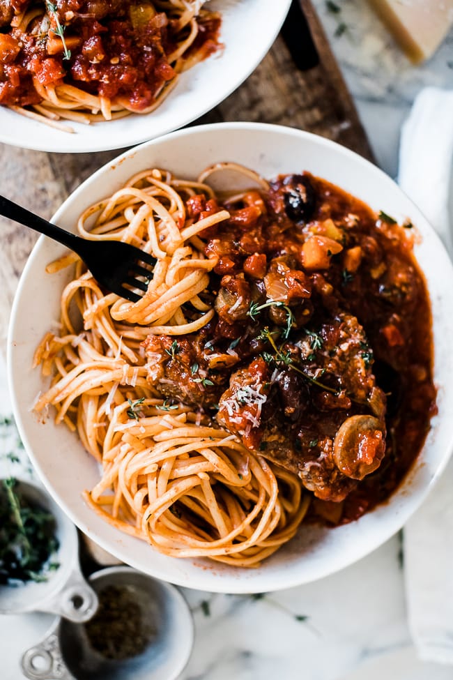 A close up of a bowl full of linguine topped with lamb cacciatore.