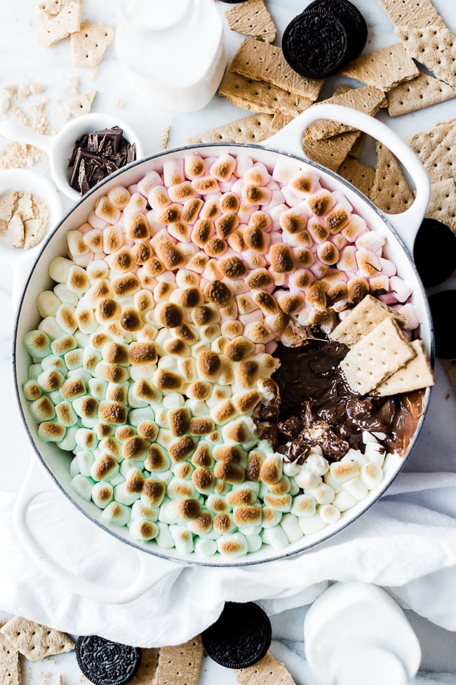 An overhead of S'mores dip recipe in a white braiser. There are 3 graham crackers dipped in.