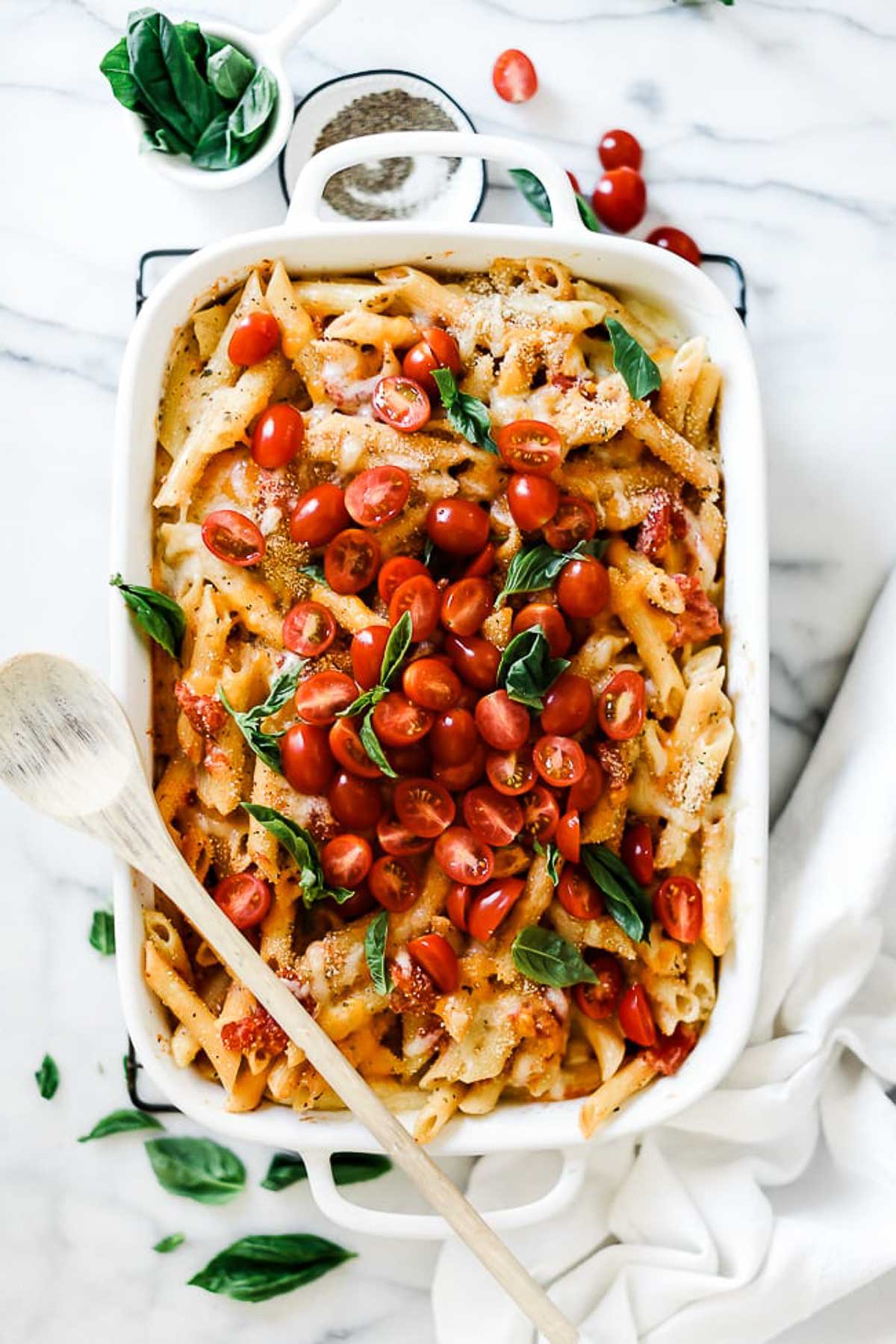 An overhead shot of a white baking pan full of Italian pasta bake garnished with basil and cherry tomatoes.