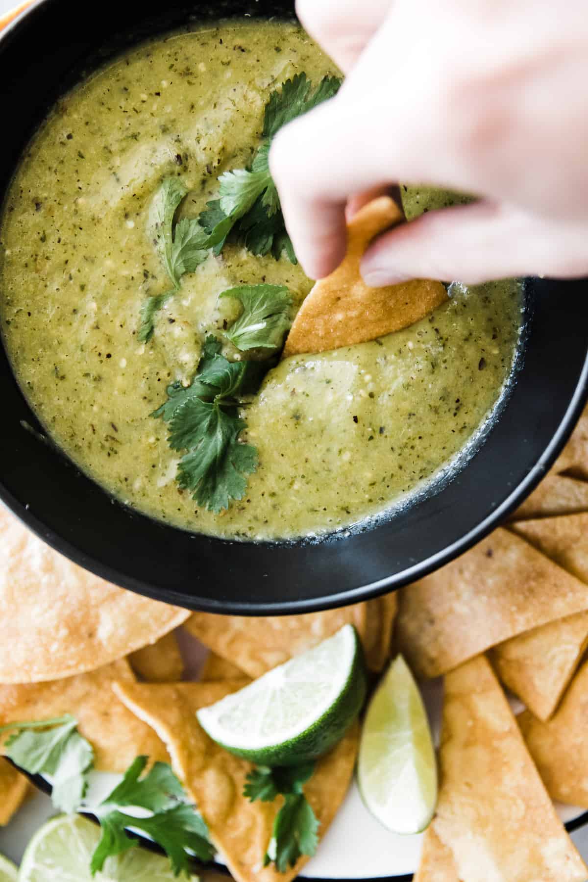 Tomatillo salsa verde in bowl with chip dipping into it.