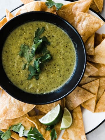 Roasted tomatillo salsa verde in black bowl with chips.