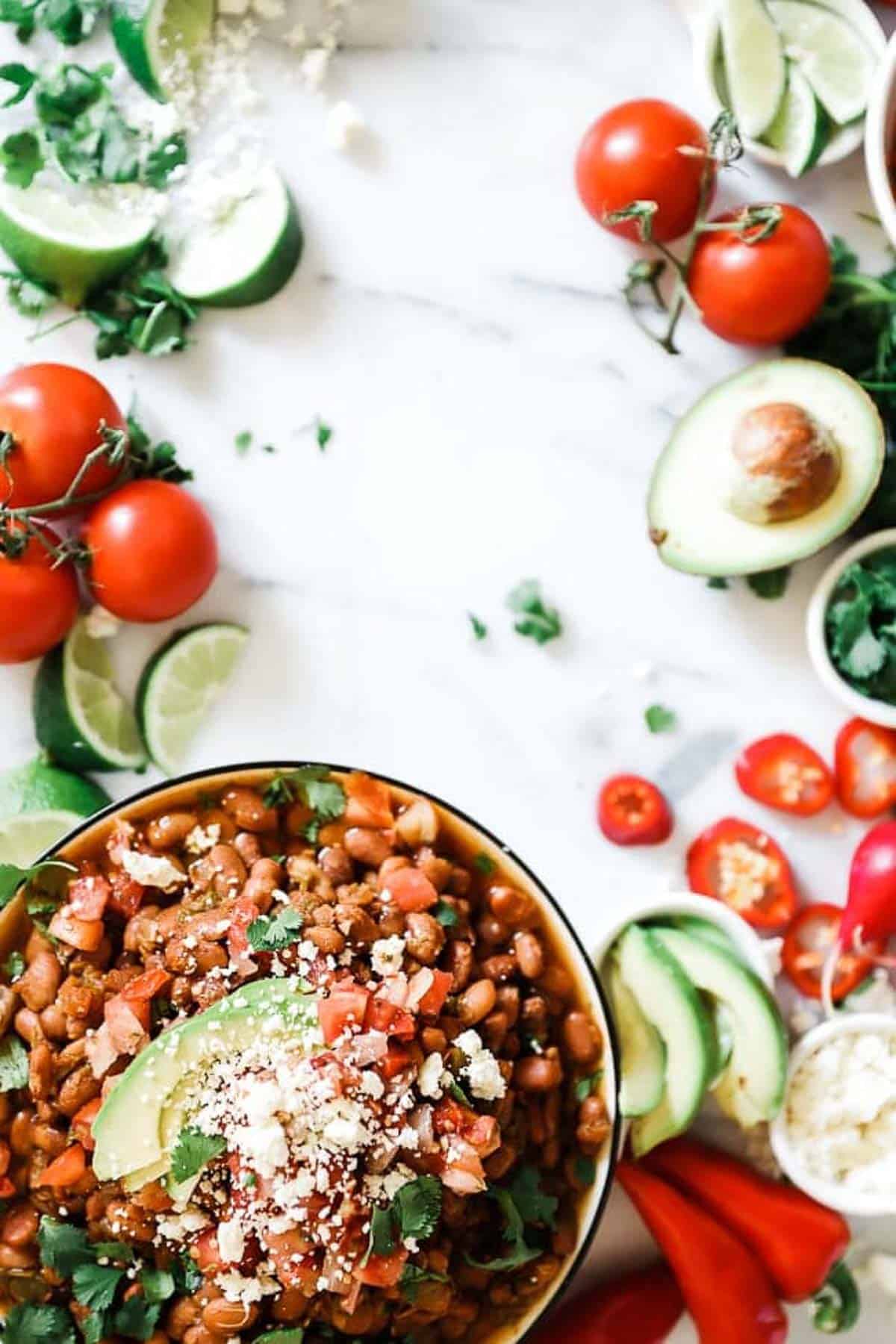 Pressure cooker pinto beans in a black rimmed bowl surrounded by tomatoes, avocado, and peppers.