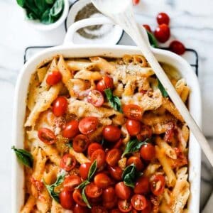 Penne pasta casserole on the table with tomatoes and basil on top.