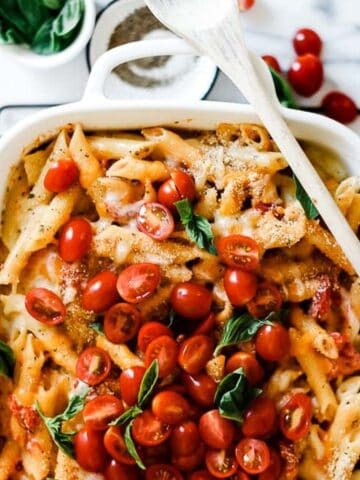 Penne pasta casserole on the table with tomatoes and basil on top.