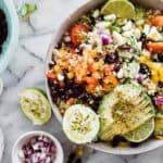 A bowl of black bean quinoa salad with squeezed lime halves and a small bowl of red onions to the side.