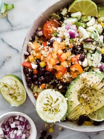 A bowl of black bean quinoa salad with squeezed lime halves and a small bowl of red onions to the side.
