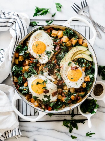 Potato hash recipe in a white braiser. It is set atop a wire cooling rack and topped with sunny side eggs.